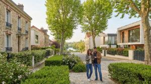 Un couple sur une rue résidentielle de Saint-Maur, avec des maisons variées et une rivière en arrière-plan, consulte une tablette.